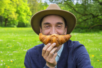 Man holding a croissant like a moustache